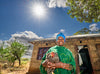 Une femme se tient devant chez elle et sourit en tenant une poule sous un beau ciel ensoleillé.