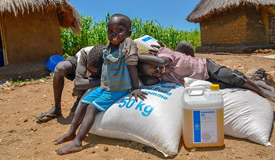 Plusieurs jeunes garçons sourient, assis ou couchés sur des sacs de nourriture et un bidon d’huile de cuisson.