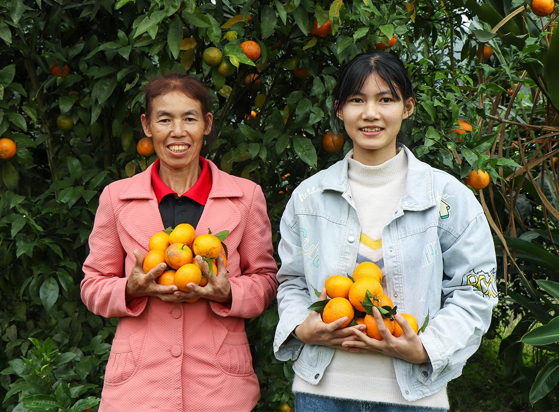 Une femme âgée et une adolescente sourient à l'objectif. Elles tiennent des oranges dans leurs mains et se tiennent devant des orangers.